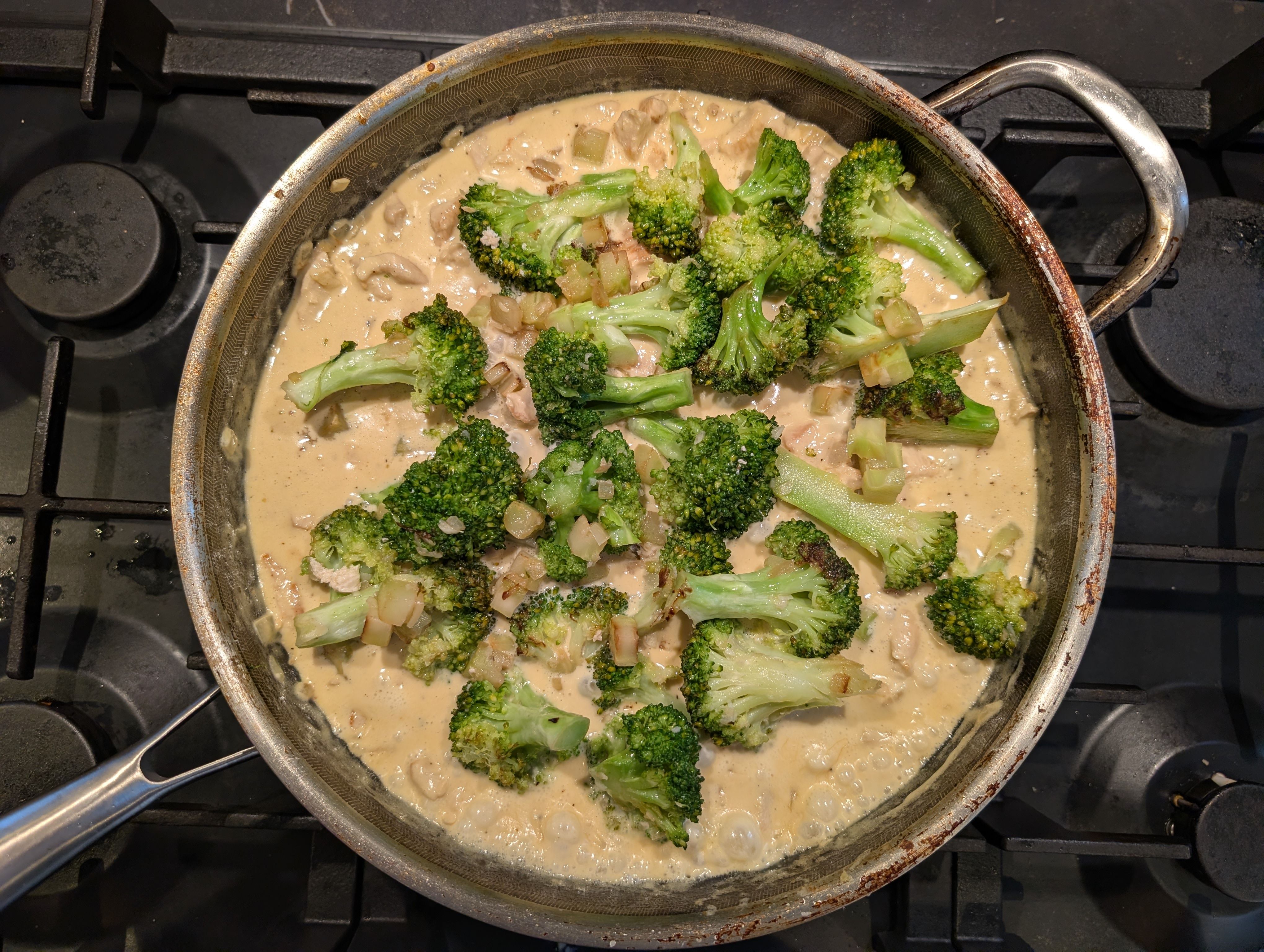 En ret med kylling i fløde samt broccolibuketter, der simrer i en pande.