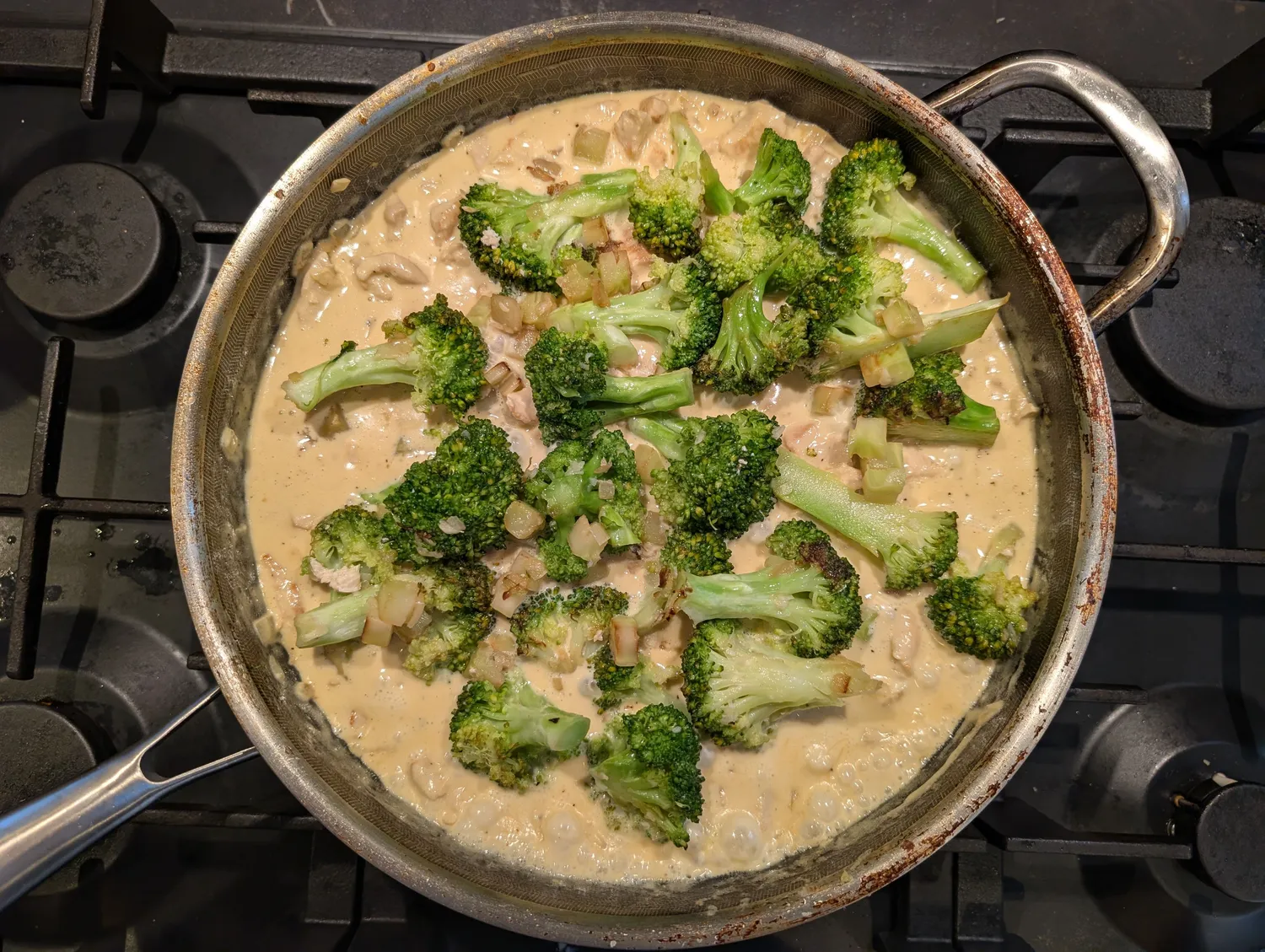 En ret med kylling i fløde samt broccolibuketter, der simrer i en pande.