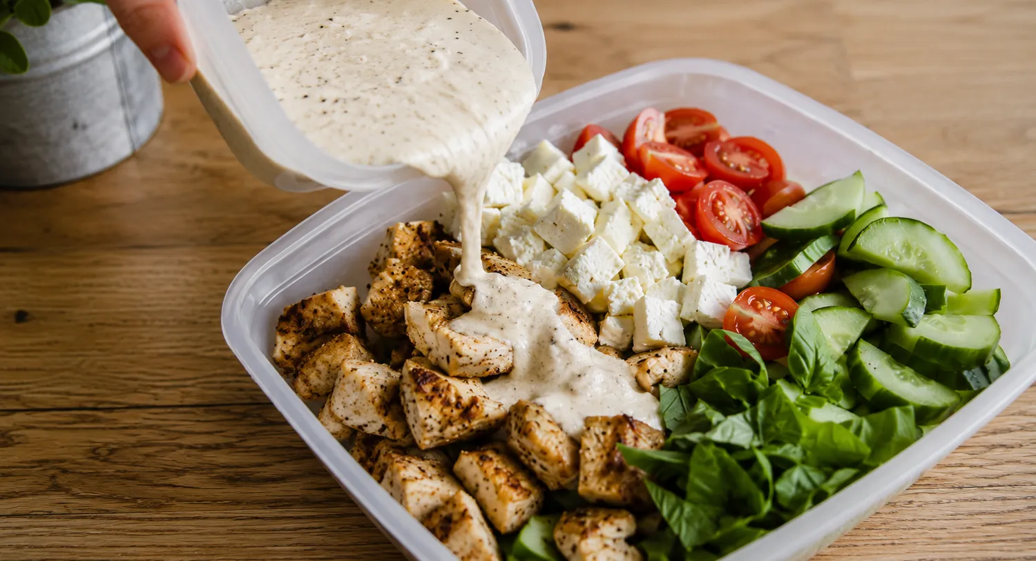 Cremet dressing med dijonsennep, græsk yoghurt og citron hældes over en hjemmelavet keto kyllingesalat med stegt kylling, feta, cherrytomater, agurk og frisk basilikum.