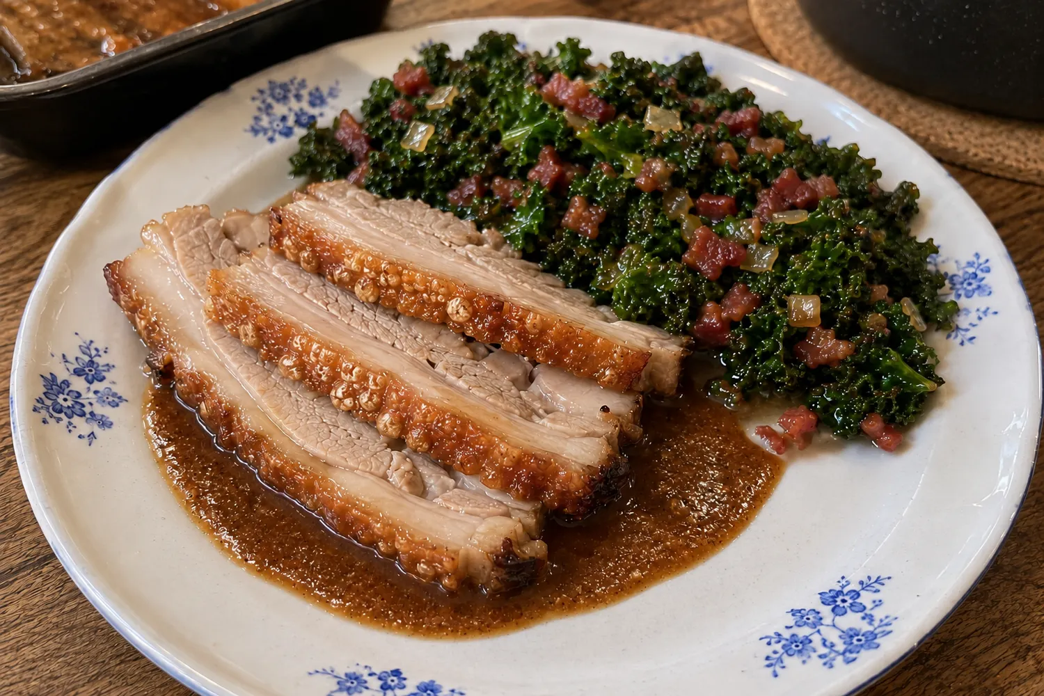 Tre skiver dansk flæskesteg med sprød svær, serveret med grønkål, små baconstykker, sauterede løg og brun keto-sauce.