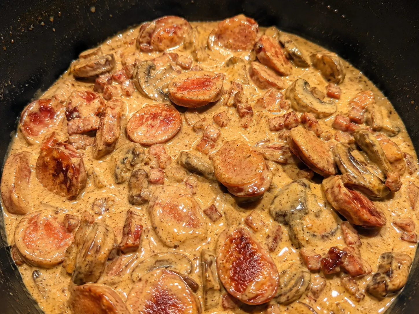 pølser og bacon simrer i cremet paprikasauce under tilberedningen af keto one pot-retten.