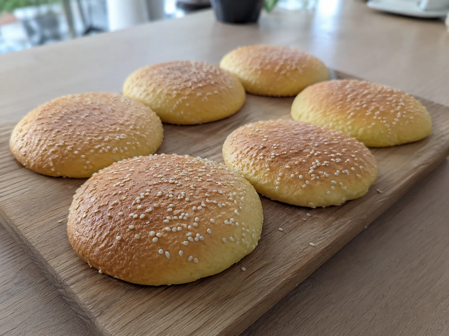 Hjemmebagte flade keto burgerboller med sesam på et træbræt i et lyst køkken.