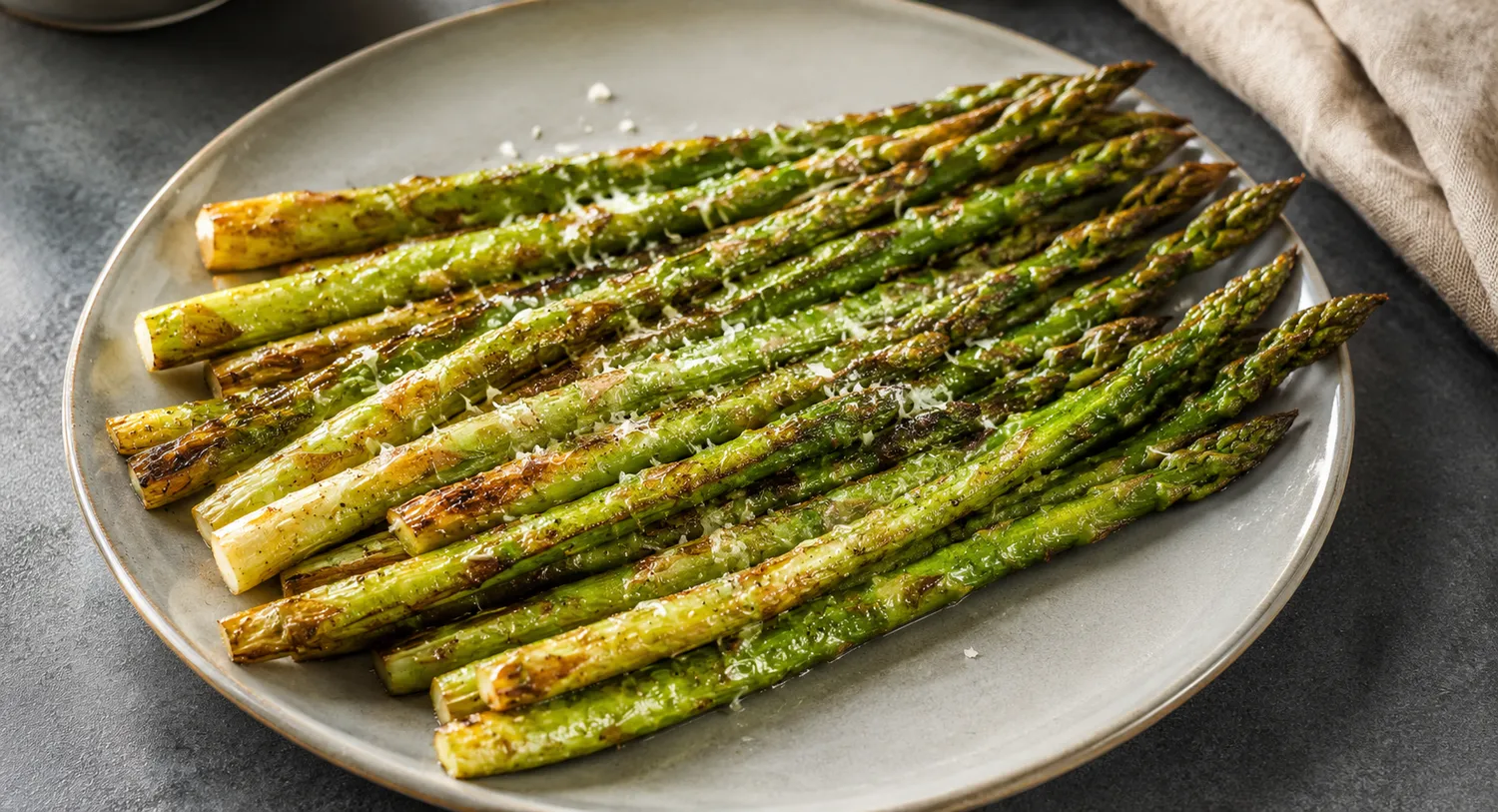 Stegte grønne asparges med gyldne kanter og friskrevet parmesan serveret på en lys tallerken.